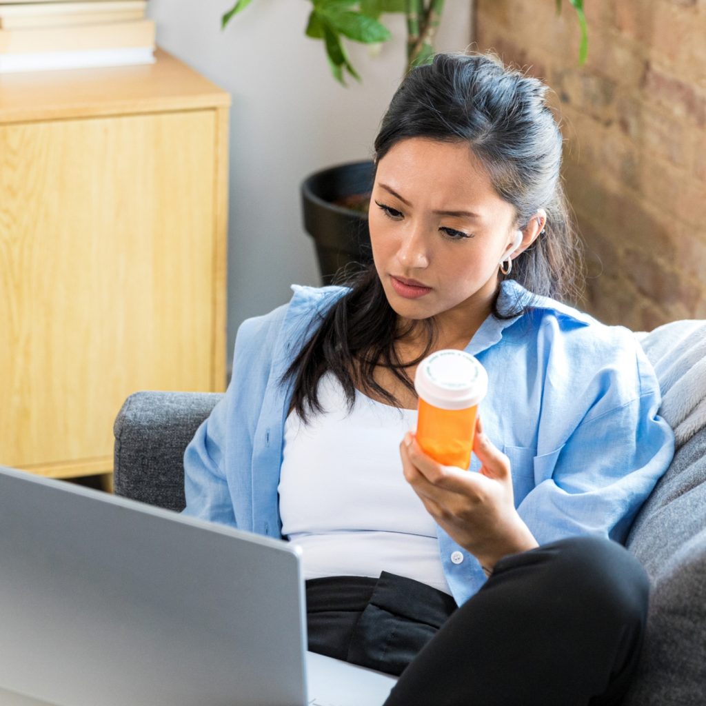 Woman holding pill bottle and looking at laptop